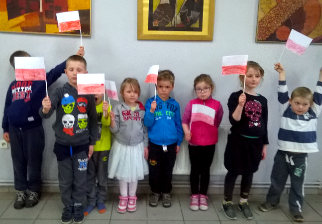 dzieci stoją w rzędzie i trzymają małe flagi Polski