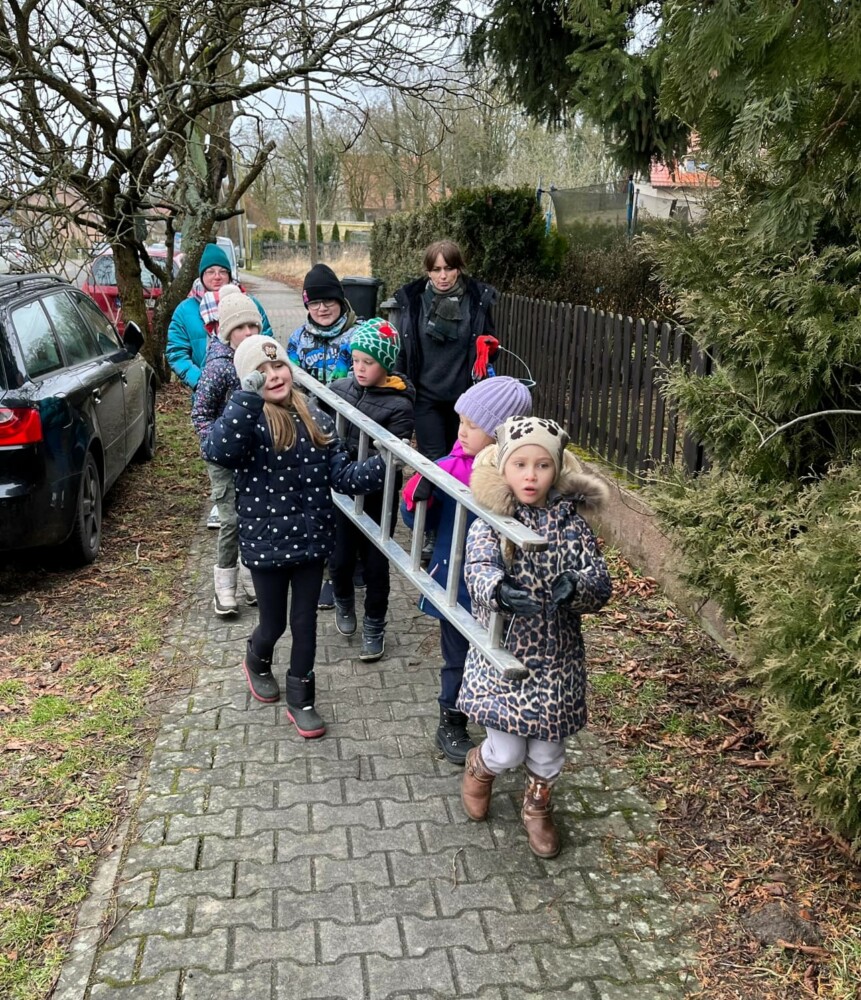 Fotografia przedstawia grupę dzieci niosących drabinę.